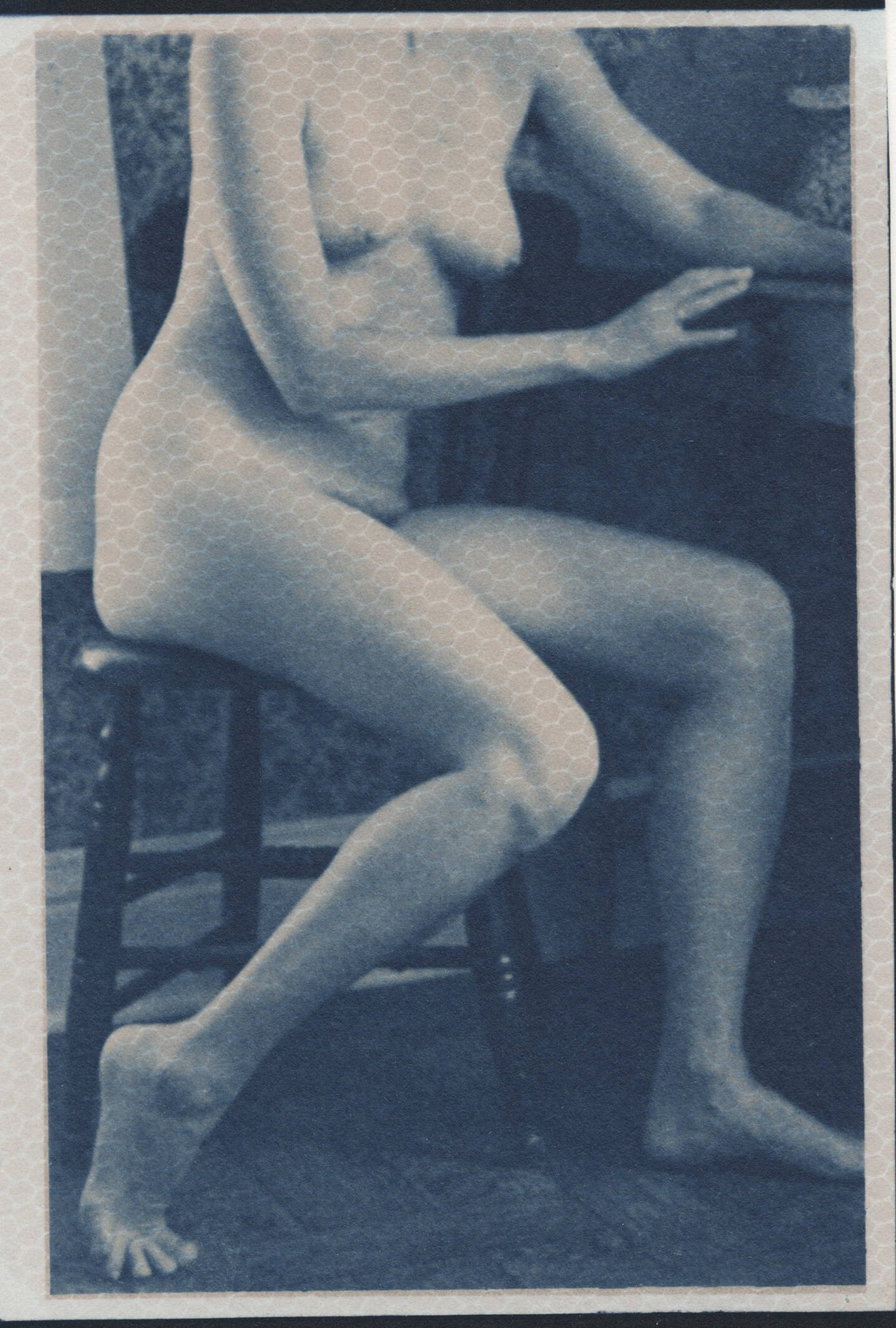 Blue cyanotype photographic image of a nude woman seated at a desk.